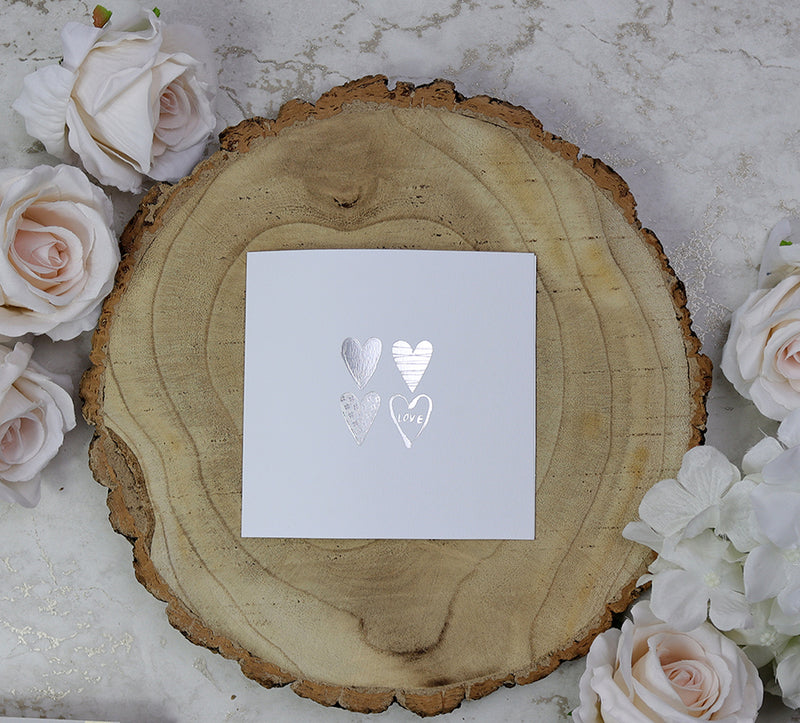 Front view of 5068 Small Square Wedding Invitation, showcasing four silver letterpress foiled hearts on a white background, priced at 50p each for affordable elegance
