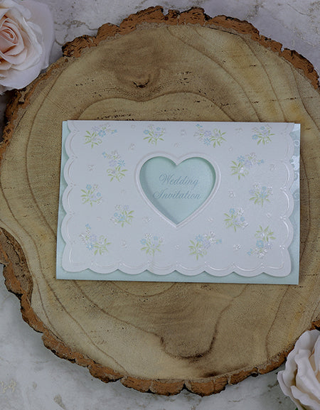 Front view of 7121 White Pearlescent Shimmer Invitation, showcasing a heart-shaped cutout and small bouquets of green and pink embossed flowers, creating a romantic and elegant design