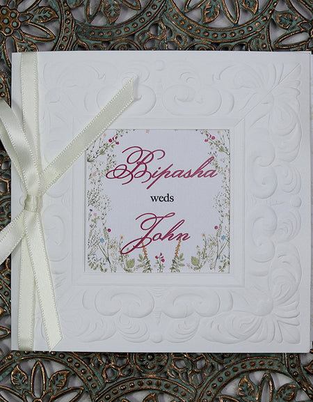 Flat-lay of 8701 square wedding invitation showcasing the satin white ribbon and elegant embossed details. From Shaadi Cards.com