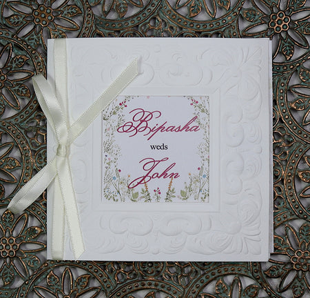 Flat-lay of 8701 square wedding invitation showcasing the satin white ribbon and elegant embossed details. From Shaadi Cards.com